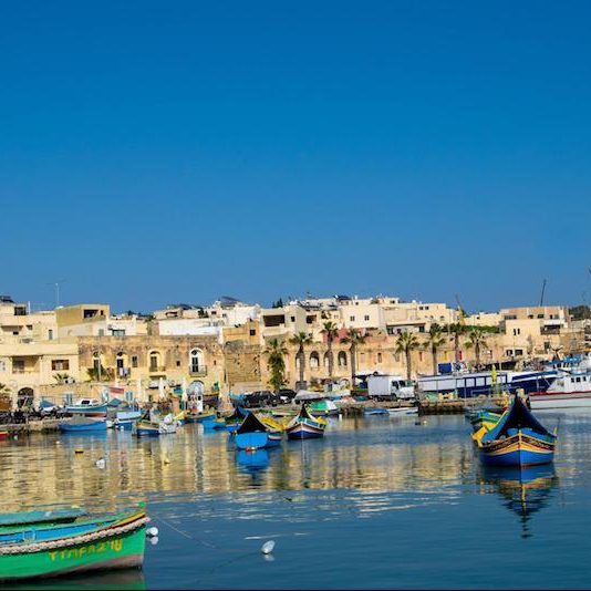 Boats in Marsaxlokk, a fishing town in Malta. This beautiful town must be included in your trip to Malta, even if you're traveling to Malta without a car! Read tips for visiting Malta without a car! #travel #Malta #Europe #Marsaxlokk