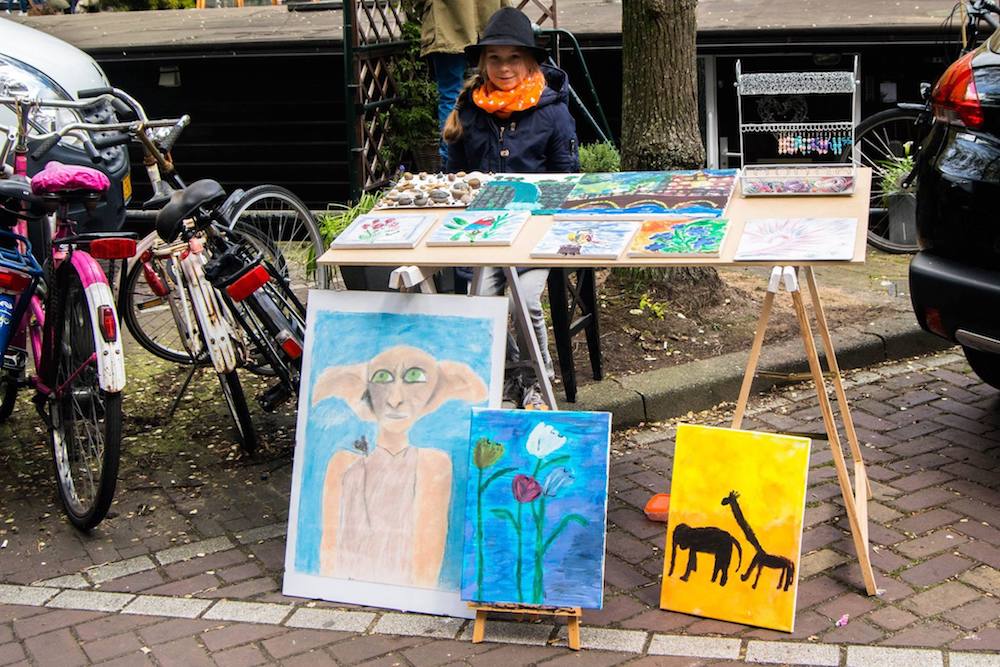 Girl selling street art on the street on King's Day in Amsterdam. Read tips for celebrating Koningsdag in Amsterdam! #Amsterdam #Netherlands