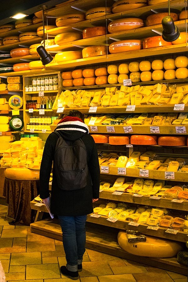 Ein Mann stöbert in einem kleinen holländischen Käseladen in Amsterdam nach holländischem Käse, einer der besten Orte, um Gouda, Edamer und andere Käsesorten zu probieren! 