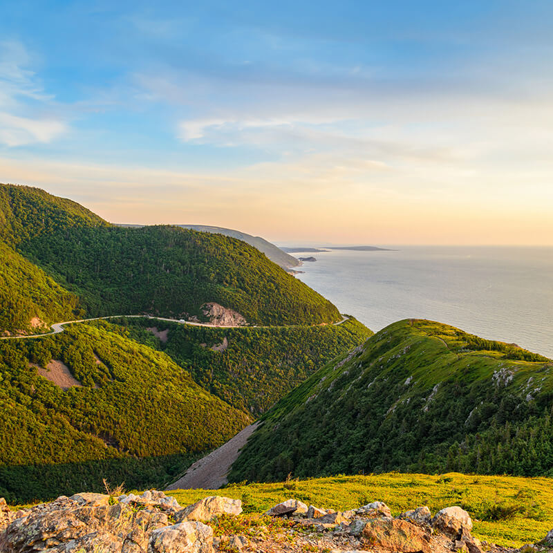 Beautiful sunset view of the Cabot Trail on Cape Breton Island in Canada, one of the most beautiful road trips in the world, with rolling hills and views of the sea! #travel