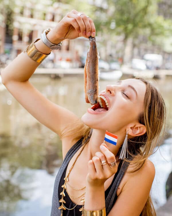Girl eating herring in Amsterdam, the Netherlands. Read about Dutch foods that you must try in Amsterdam, the Netherlands! #travel #netherlands #holland #amsterdam