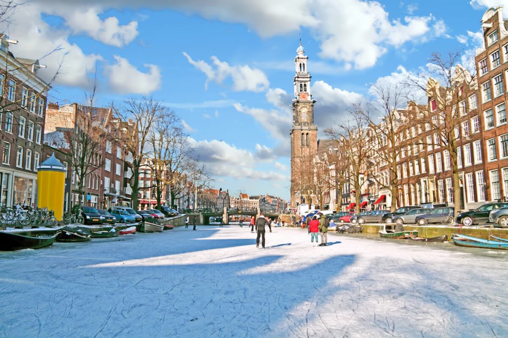 People ice skating in Amsterdam in winter. It's very rare that canals in Amsterdam freeze, but ice skating is one of the best things to do in Amsterdam in winter! #travel #amsterdam