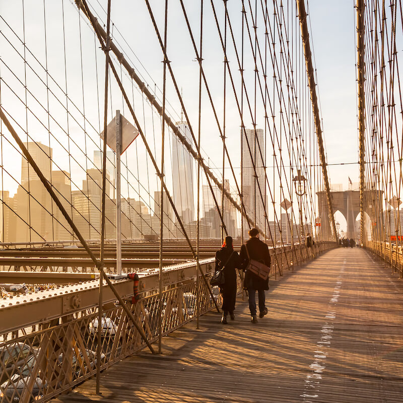 Couple walking over Brooklyn Bridge from Manhattan to Brooklyn. Read about what to do in downtown Brooklyn in this insider guide to downtown Brooklyn! #travel #brooklyn #NYC