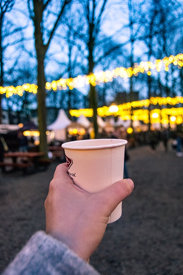 Gluhwein cup with the Royal Christmas Market in the Hague in the background.  Read about attending this Dutch Christmas market in Holland! #travel #holland #christmas #netherlands