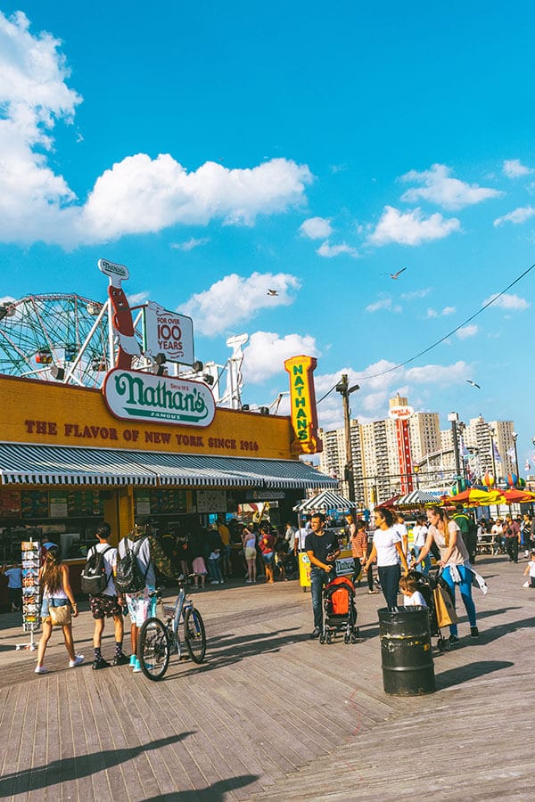 People walking on the Coney Island boardwalk past Nathan's Famous Hot Dogs in Brooklyn, New York