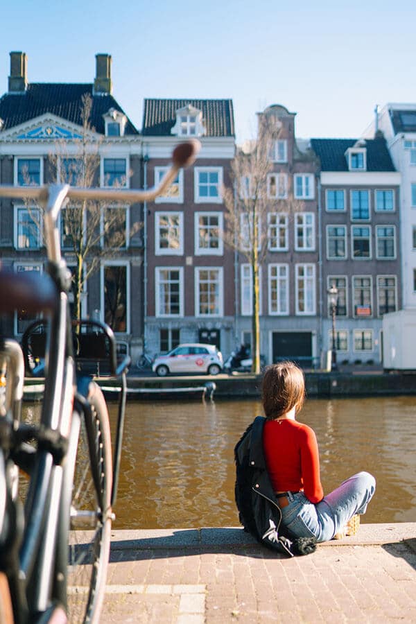 Girl enjoying solo travel in Amsterdam while sitting along Amsterdam canals!