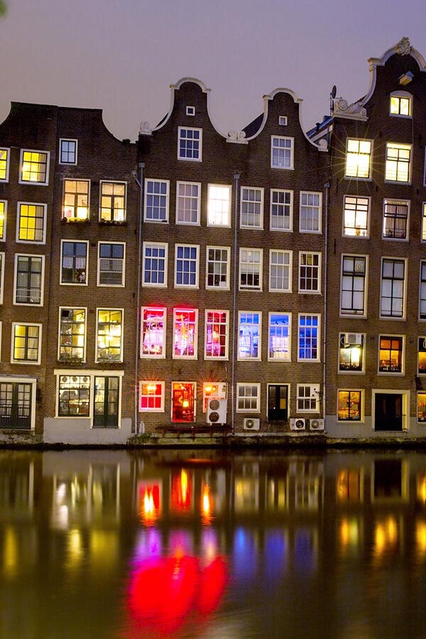 Red lights and canal houses lit up at night within the Red LIght District in Amsterdam.