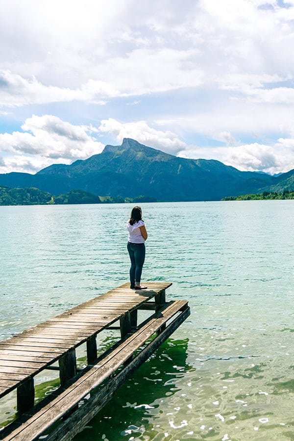 Girl admiring the beautiful view of the mountains by alpine lakes in Austria.  Read about how to save money on hotels in Austria. #travel #austria #europe