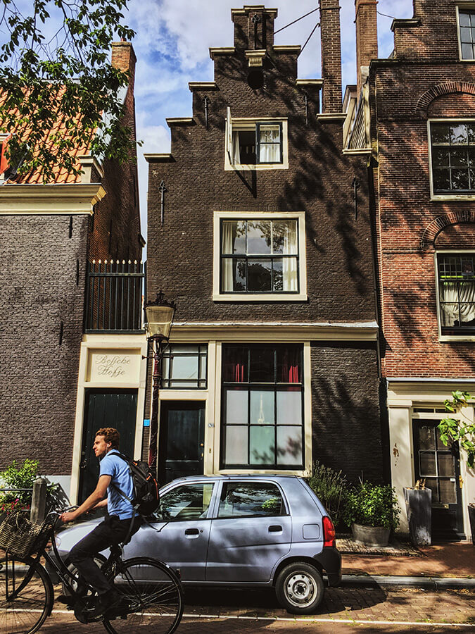 Man biking past a beautiful hofje in Amsterdam.  Follow this self-guided walking tour of the Jordaan to see secret spots in the Jordaan! #travel #amsterdam #holland #netherlands #nederland