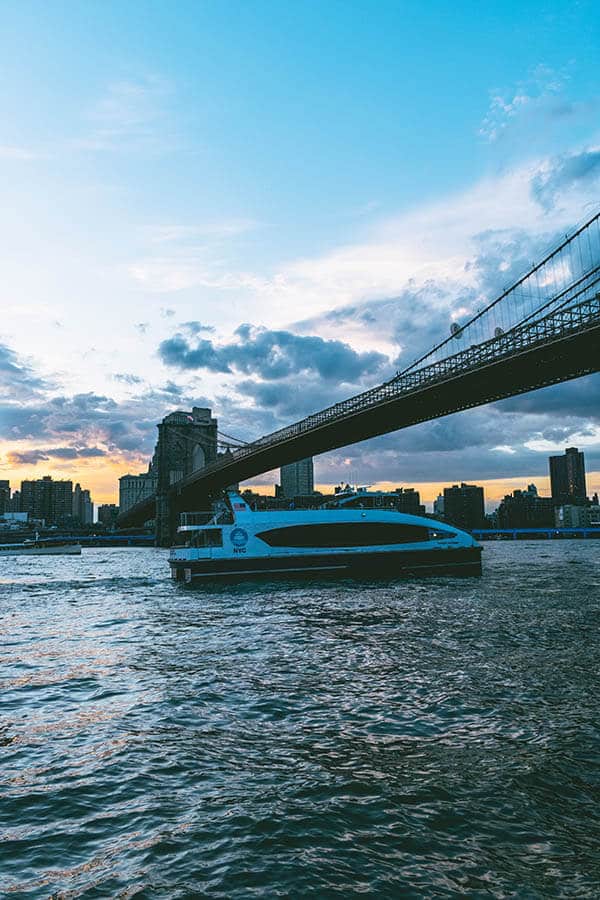 New York ferry sailing underneath the Brooklyn Bridge with stunning views of Manhattan at sunset