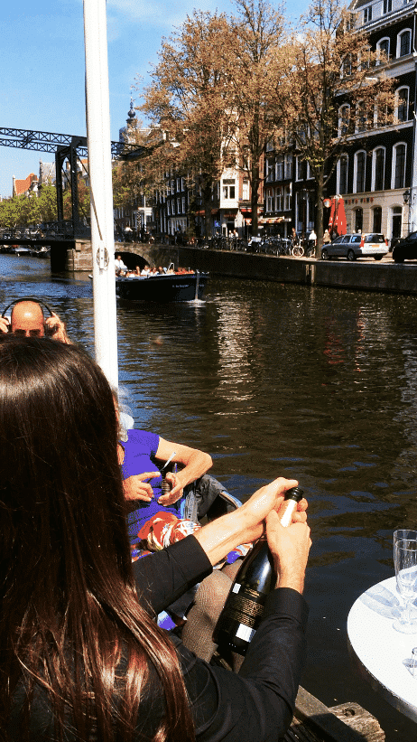 Couple opening a bottle of champagne along the canals of Amsterdam; This is one of the most romantic things to do in Amsterdam! #amsterdam #travel 